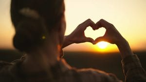 Hands forming a heart at sunset symbolizing faith and love